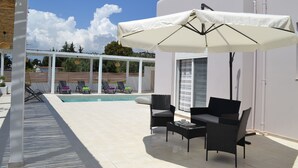 A poolside area with a covered seating area, a pool, and lounge chairs.