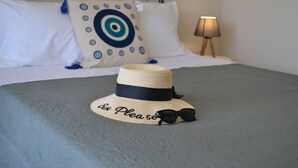 A bed with a grey bedspread, a straw hat with "Six please" text, and black sunglasses on the bed.