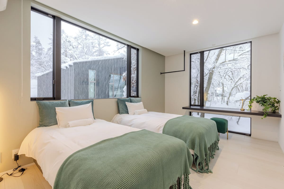 Habitació d'hotel moderna amb dos llits, finestres grans, una petita zona de seients i vista a un paisatge nevado.