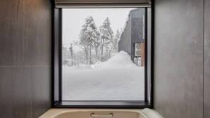A bathroom with a bathtub, a window with a view of a snowy landscape and trees. - Origami Twins (Hakuba)