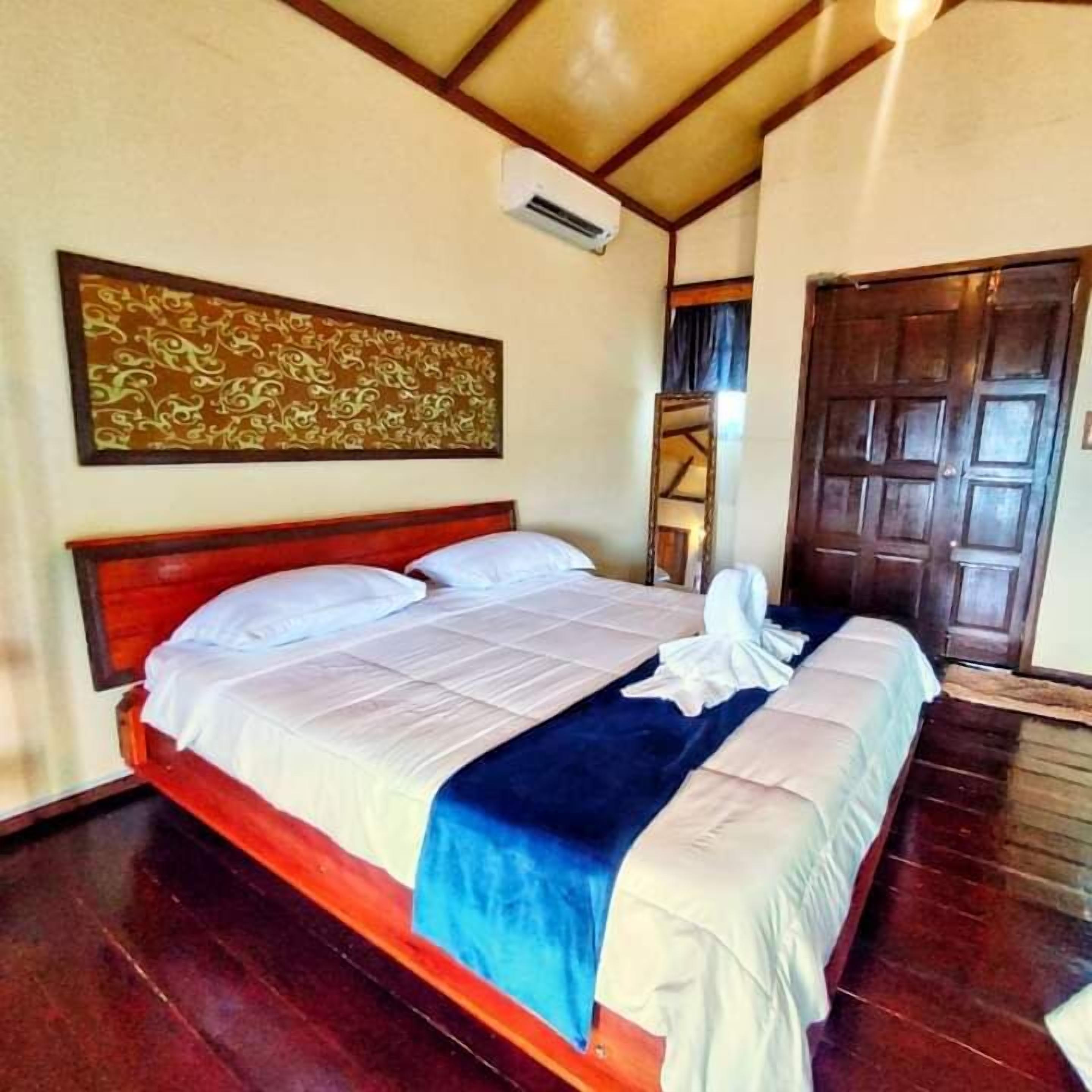 A hotel room with a wooden bed, a large decorative wall piece, and a wooden door.