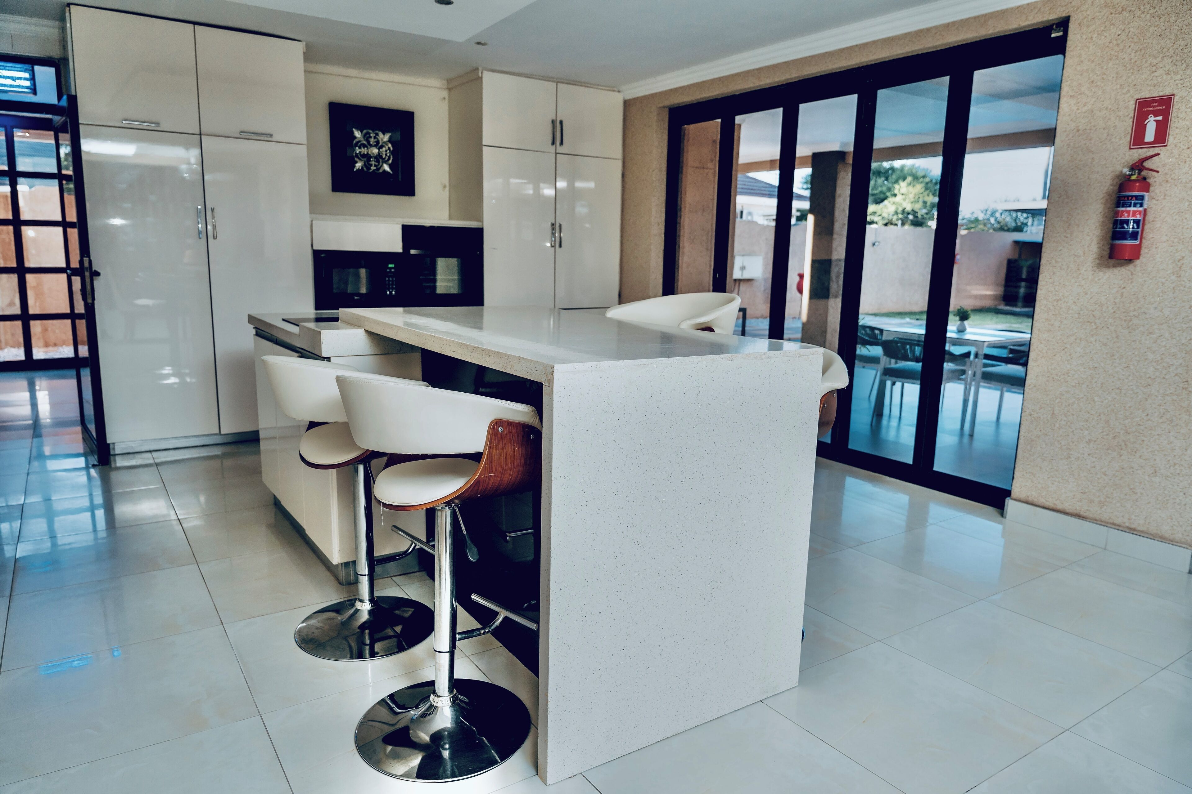 A modern kitchen with white cabinets, a central island with bar stools, a microwave, and a fire extinguisher on the wall.