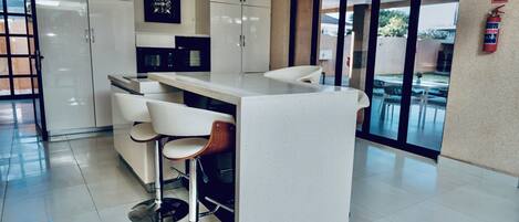 A modern kitchen with white cabinets, a central island with bar stools, a microwave, and a fire extinguisher on the wall.