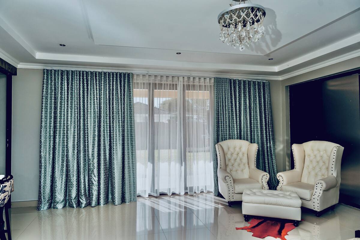 A spacious living room with a large window, two plush armchairs, a chandelier, and a red rug.