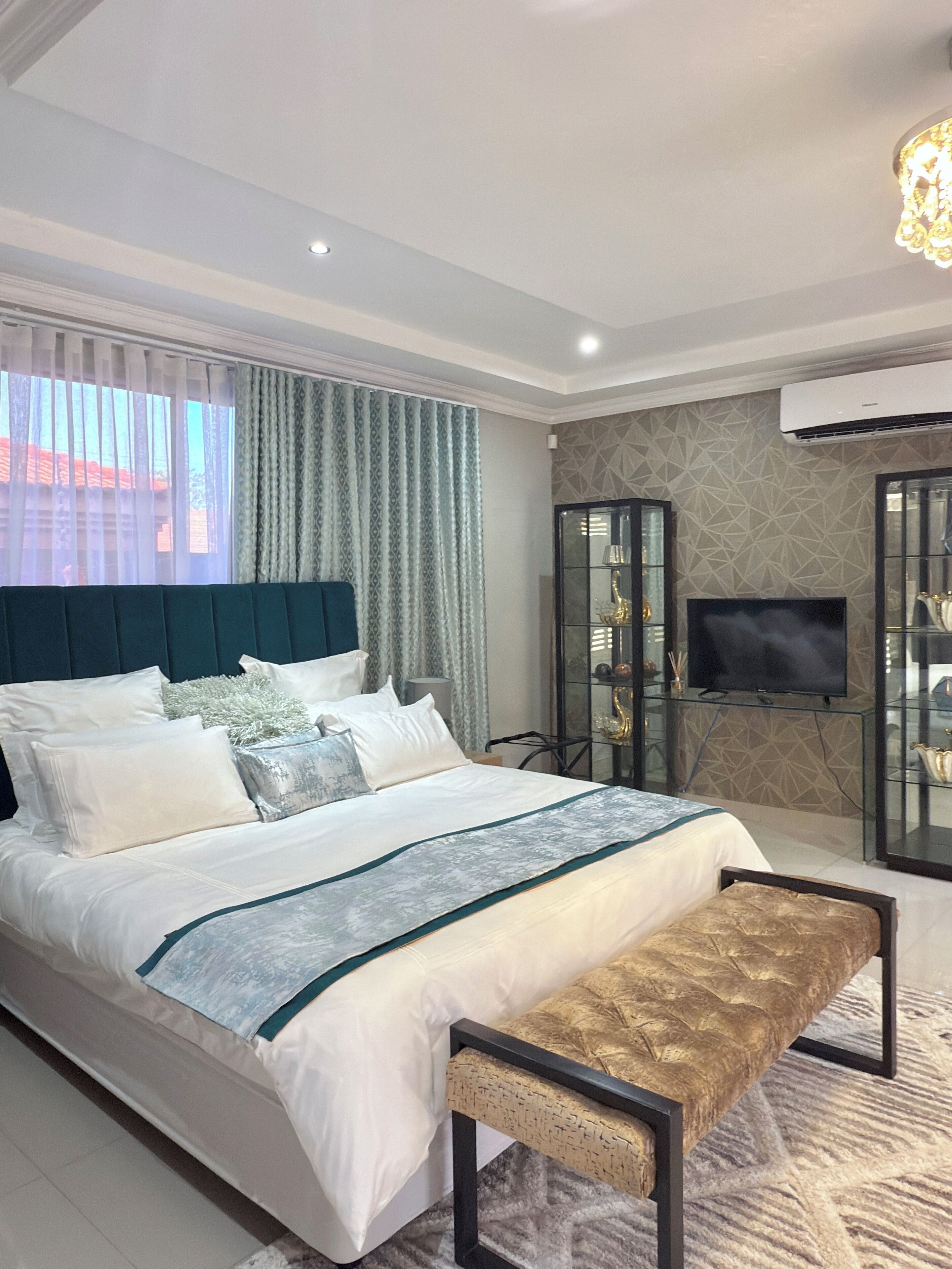 A modern bedroom with a large bed, a bench, a TV, and a glass cabinet.