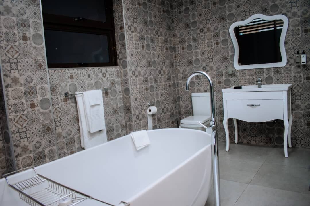 A bathroom with a freestanding bathtub, a white vanity with a mirror, and patterned stone walls.
