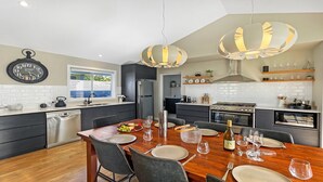 A modern kitchen with a dining area, featuring a wooden table set for a meal, a stainless steel refrigerator, and a built-in oven. - FIGTREE RETREAT - THE VINTAGE HOLIDAY HOUSES (POKOLBIN)
