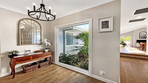 A spacious entryway with a large sliding glass door leading to a garden, a wooden console table with baskets, a mirror, and a chandelier. - FIGTREE RETREAT - THE VINTAGE HOLIDAY HOUSES (POKOLBIN)