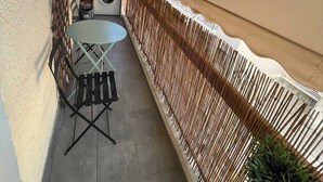 Een klein balkon met een tafel, stoelen, een wasmachine en een hek.