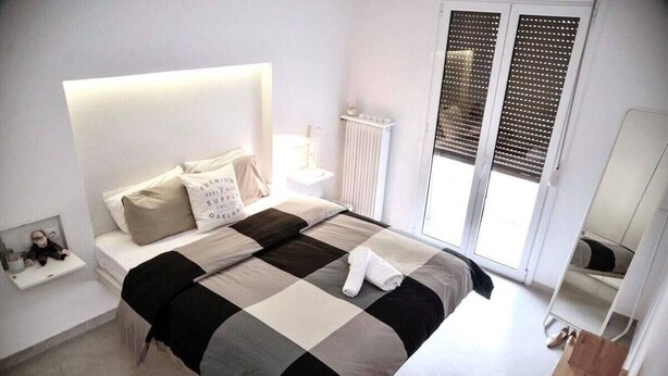 Een moderne slaapkamer met een groot bed, een nachtkastje, een radiator en een raam met jaloezieën.