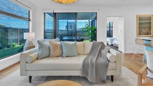 A modern living room with a sofa, a coffee table, and a view of a fenced outdoor area. - Birdsong Beach Retreat (Skennars Head)