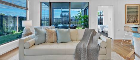 A modern living room with a sofa, a coffee table, and a view of a fenced outdoor area.