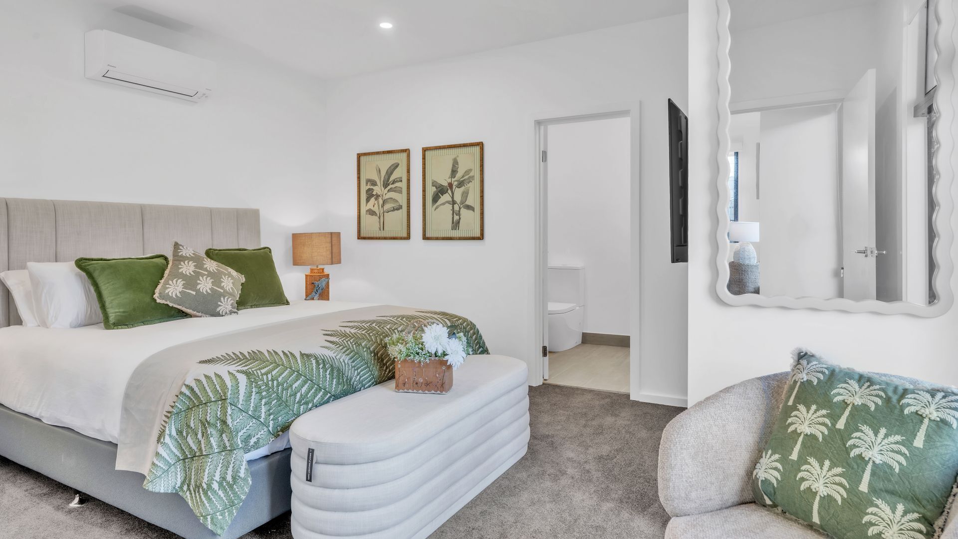 A modern bedroom with a bed, bedside table, lamp, and a mirror.