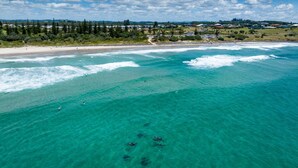 An aerial view of a coastal area with clear turquoise waters, a sandy beach, and a backdrop of residential buildings and greenery. - Birdsong Beach Retreat (Skennars Head)