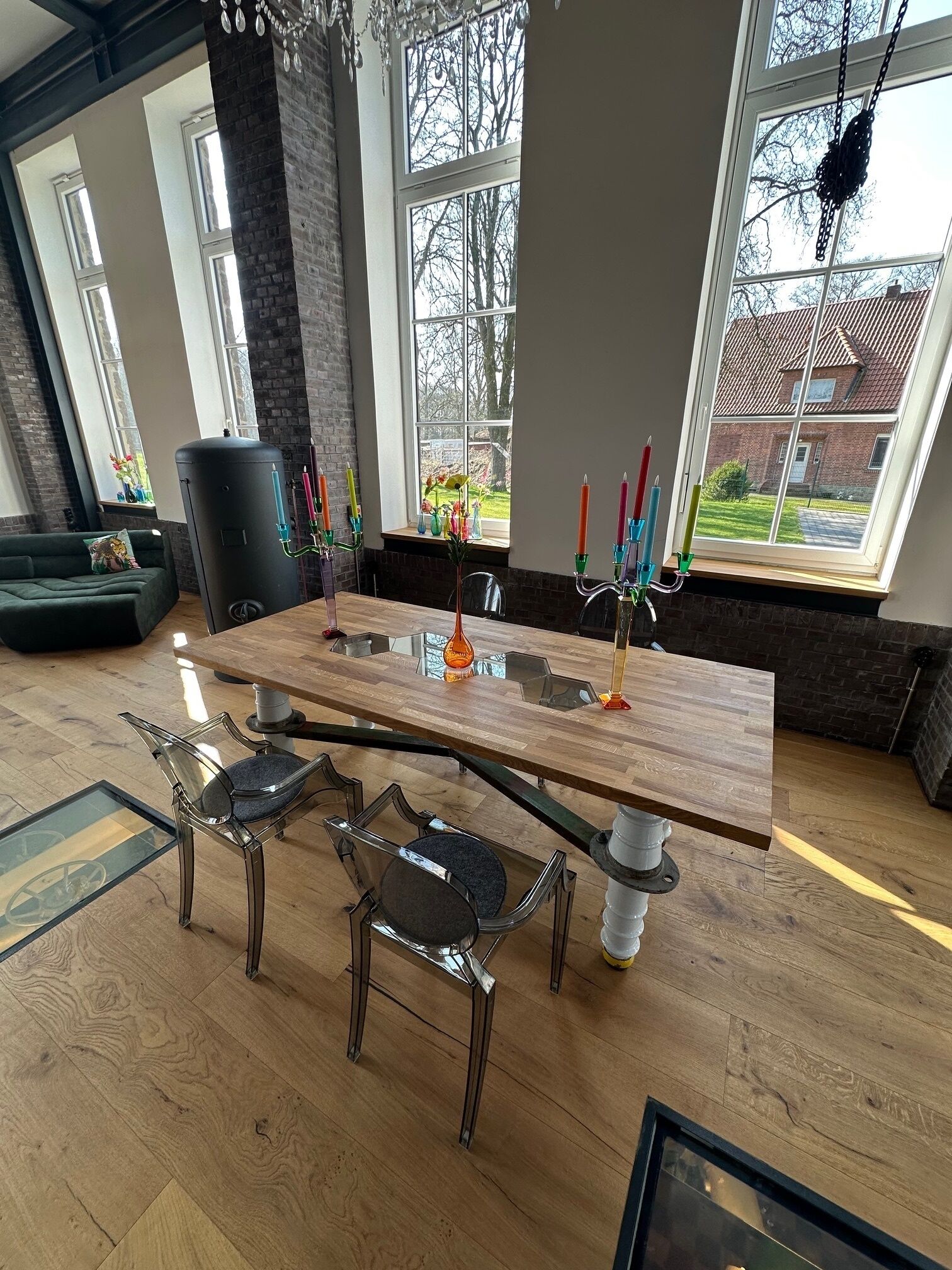 A modern dining area with a wooden table, clear chairs, and a view of a brick building through large windows.