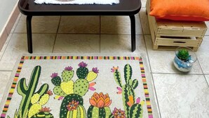 Una pequeña mesa con un mantel tejido y una vela de vidrio, sobre una colorida alfombra tejida con motivos de cactus.