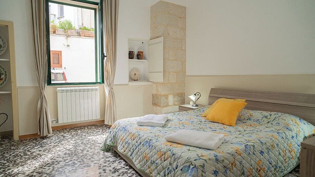 Un dormitorio con cama, ventana, pared de piedra y radiador.