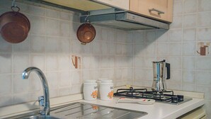 Una cocina con un lavamanos de acero inoxidable, una estufa a gas, ollas de cobre colgadas y frascos de almacenamiento blancos.