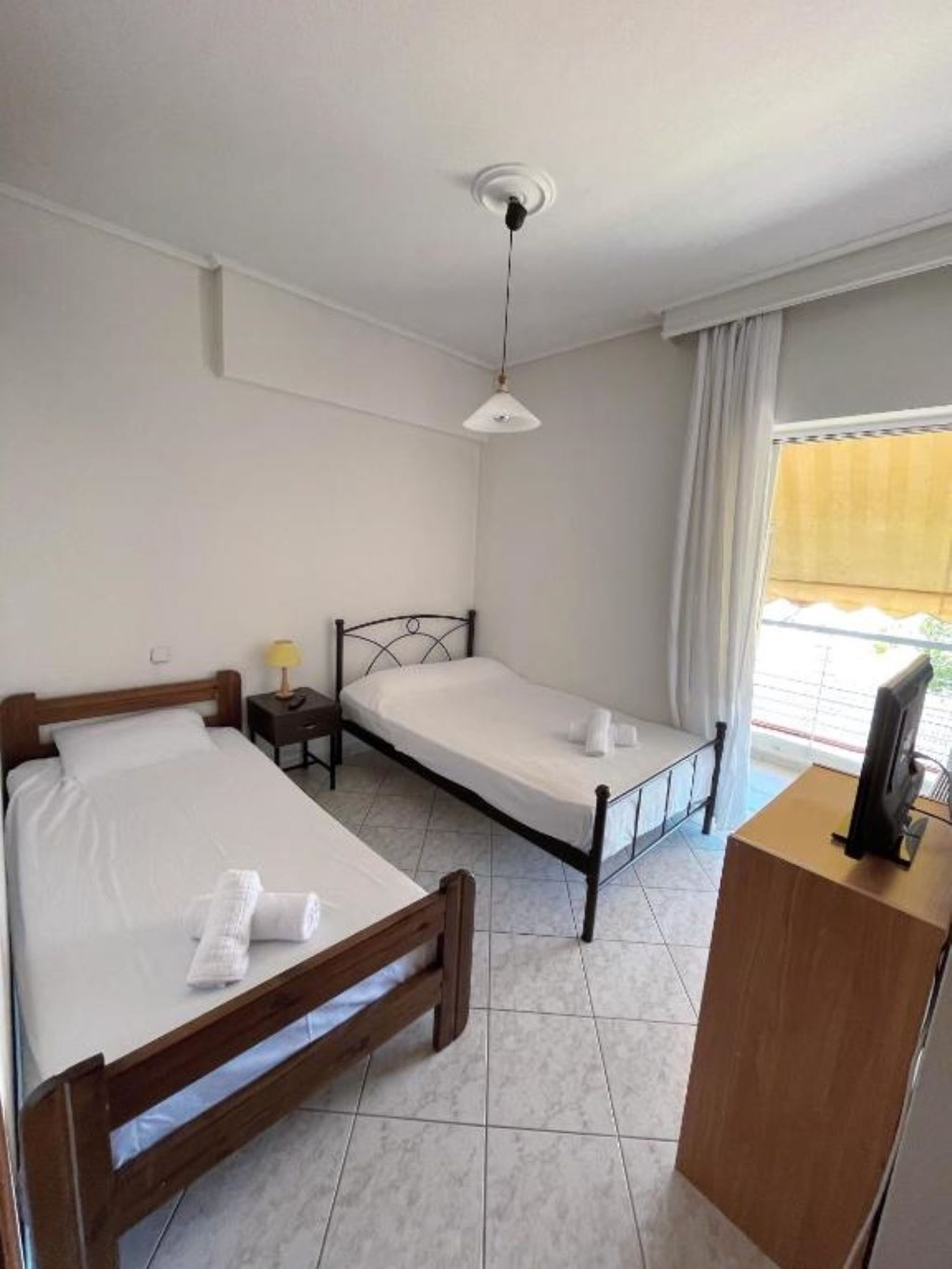 A room with two beds, a desk, a lamp, and a TV.