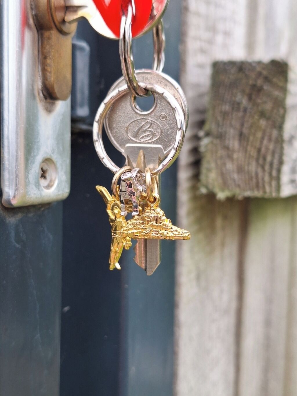 Um chaveiro com uma chave e uma pequena figura dourada presa a um porta-chaves de metal.