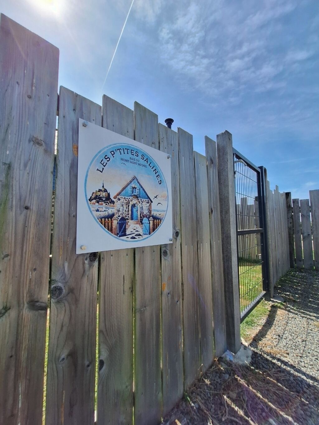 A wooden fence with a sign that reads "LES P'tites Salines" and depicts a building with a blue roof.