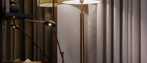 A modern hotel room with a desk, a lamp, a chair, and a mirror.