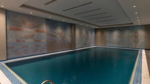 Una piscina interna con acqua cristallina, circondata da pareti decorate con murales artistici.