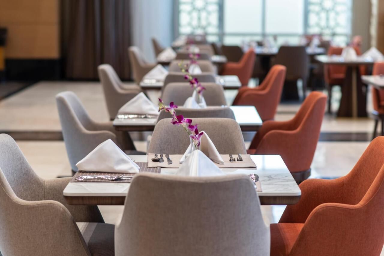 A restaurant with rows of tables and chairs, each set with a napkin, cutlery, and a vase of flowers.