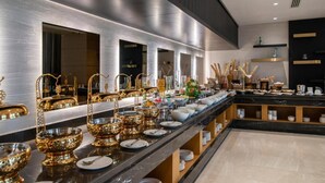 Un'attrezzatura per buffet con un'ampia scelta di piatti e posate, tra cui ciotole e piatti dorati, disposti su un lungo bancone.
