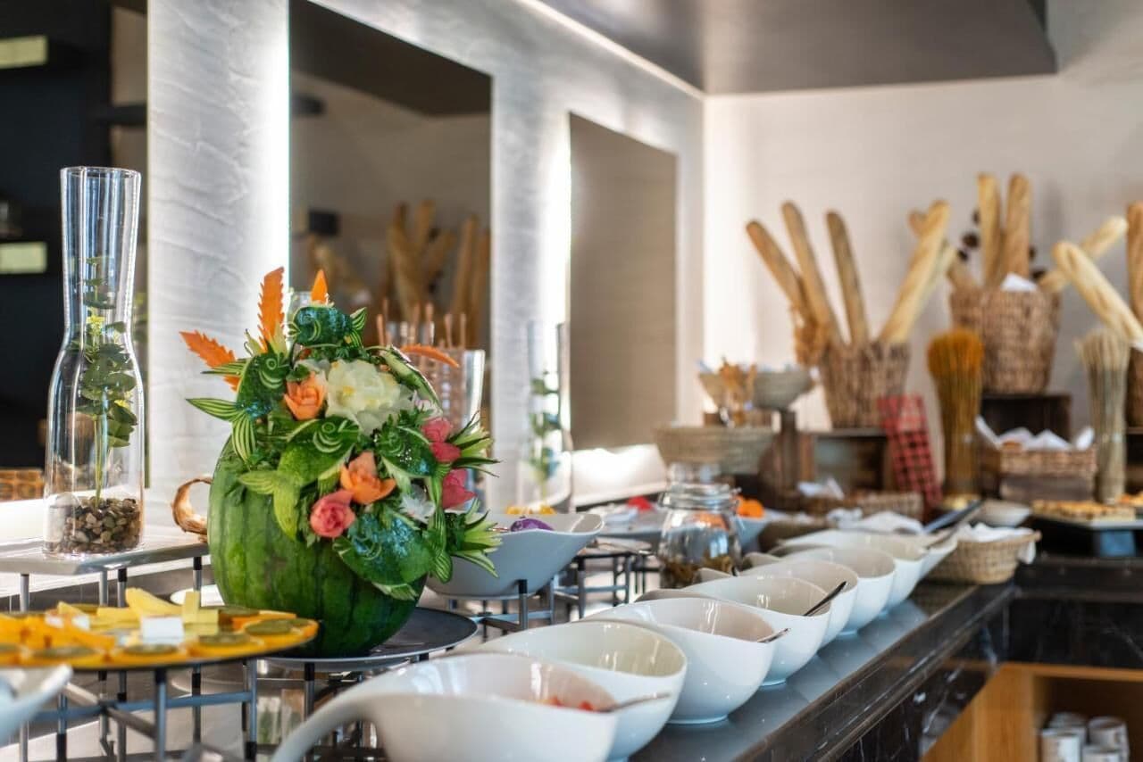 A buffet setup with a large floral centerpiece, white bowls, and various food items.