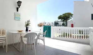 A balcony with a white railing, a table with chairs, and a view of the sea.