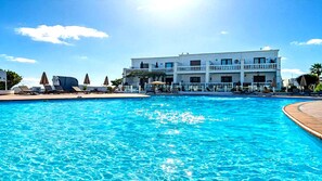 A hotel with a swimming pool, sun loungers, and a white building with balconies.