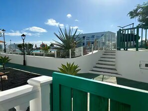 Una terraza en la azotea con piscina, palmeras y una escalera que lleva a un nivel superior.