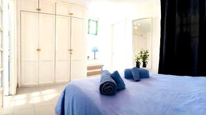 A bedroom with a bed, a wardrobe, a mirror, a lamp, and a window with curtains.