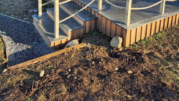A small, wooden cabin with a deck and a glass door, surrounded by a fenced area and a natural landscape. - Superior Glamping pods, in prime location along the NC500. (Scourie)