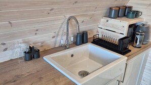 A kitchen with a white sink, wooden countertop, and cabinets. There are black mugs and a coffee maker on the counter. - Superior Glamping pods, in prime location along the NC500. (Scourie)