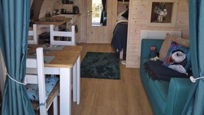 A cozy cabin interior with a wooden dining table, a sofa, and a small kitchen area. - Superior Glamping pods, in prime location along the NC500. (Scourie)