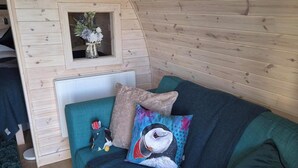 A cozy room with a wooden sloped ceiling, a teal sofa with decorative pillows, and a small wooden shelf with a plant. - Superior Glamping pods, in prime location along the NC500. (Scourie)