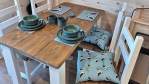 A wooden dining table with four chairs, a green first aid bag, and a blue cushion with bird patterns on the seat. - Superior Glamping pods, in prime location along the NC500. (Scourie)