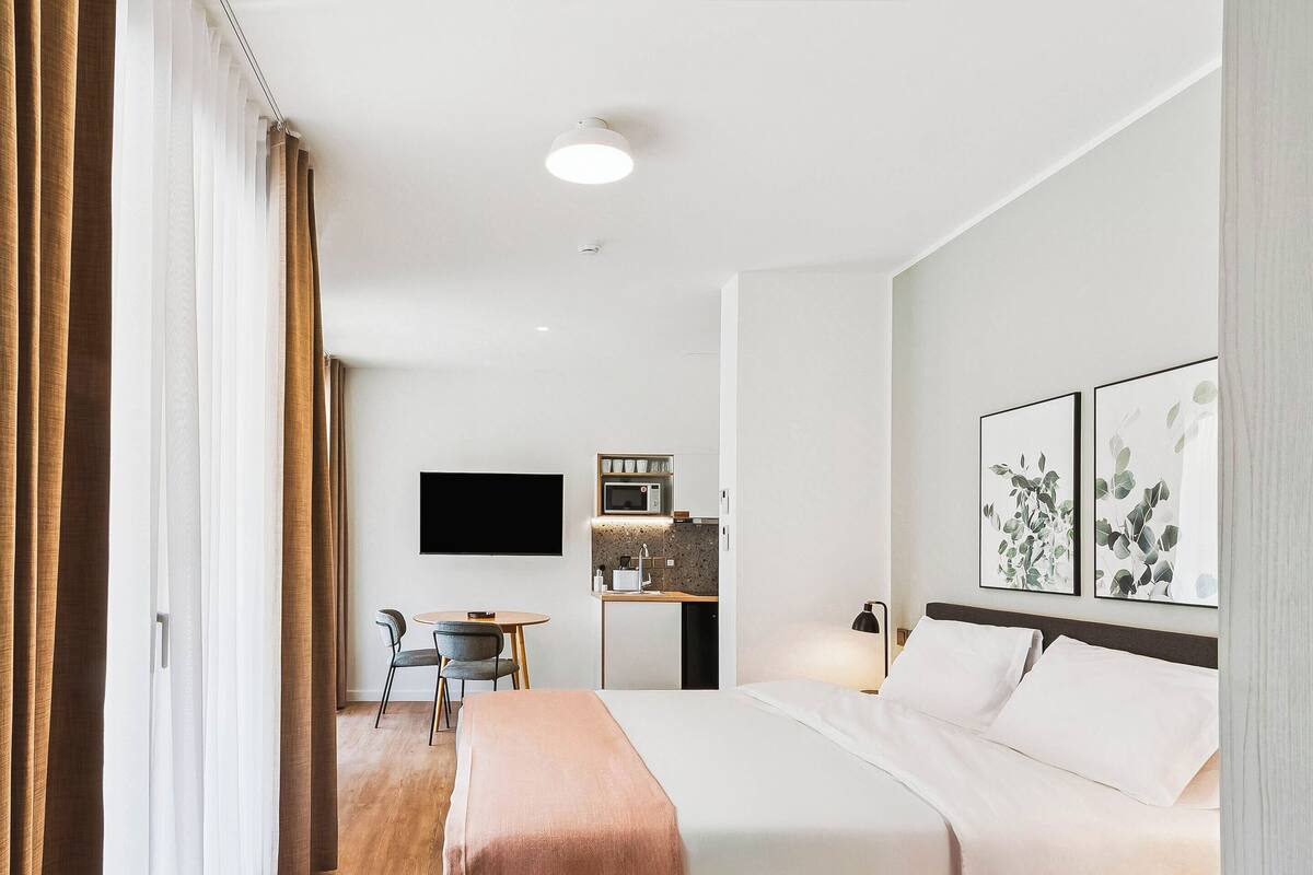 Hotellihuone, jossa on sänky, työpöytä, jossa on mikroaaltouuni, televisio ja taideteoksia seinällä.