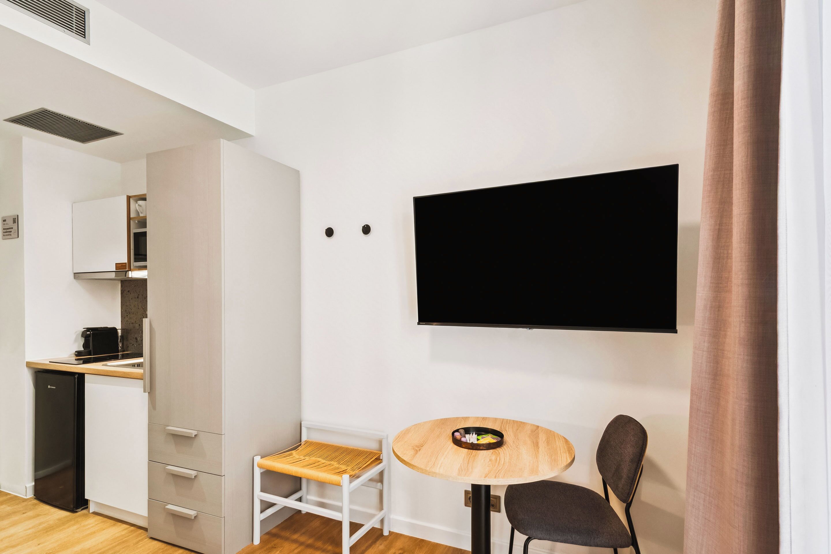 A modern room with a kitchen area, a dining table with two chairs, and a flat-screen TV mounted on the wall.