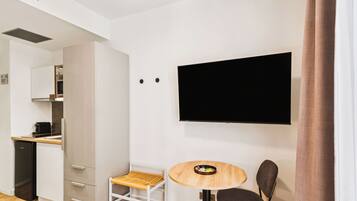 A modern room with a kitchen area, a dining table with two chairs, and a flat-screen TV mounted on the wall.