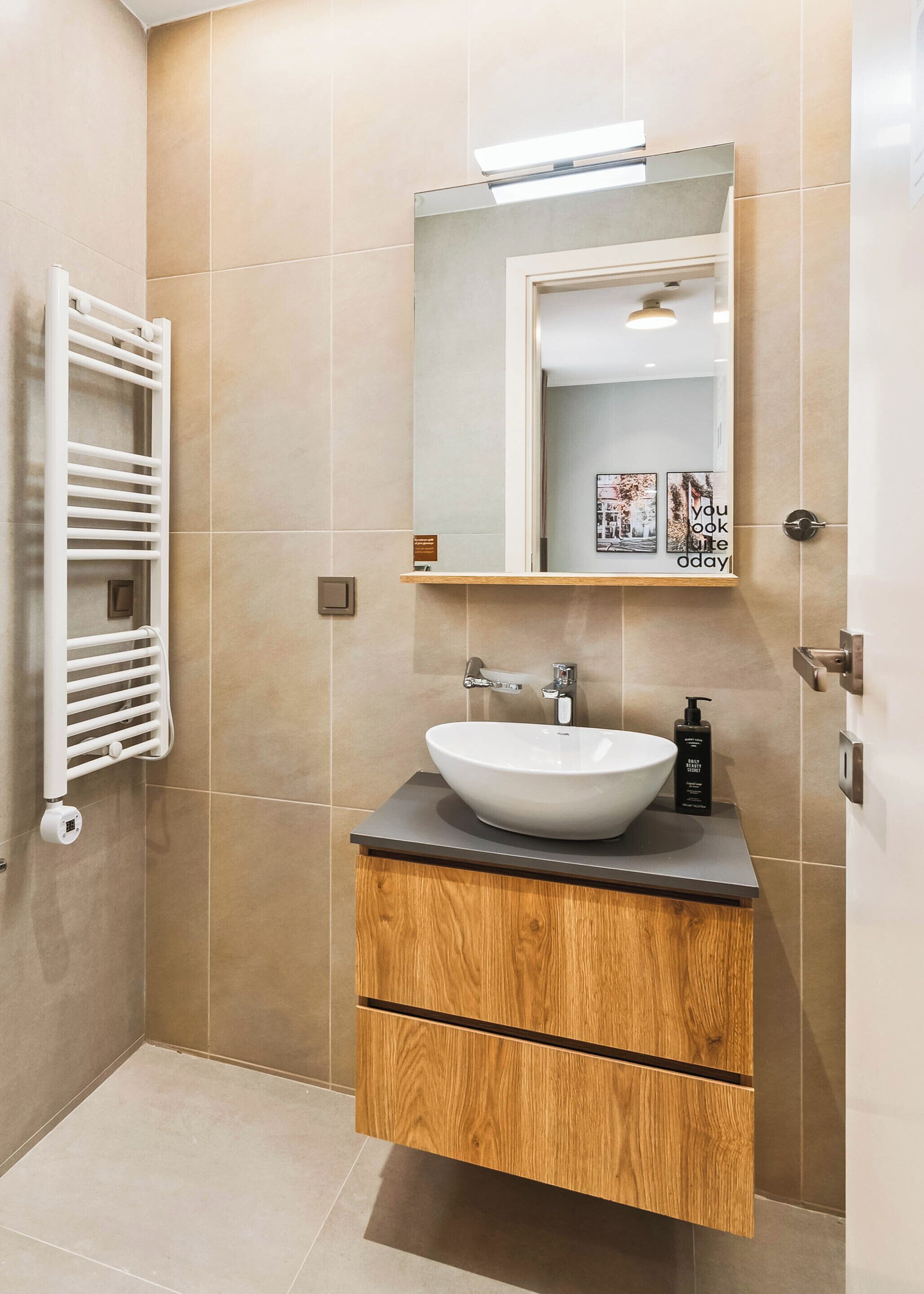 A modern bathroom with a white sink, wooden vanity, and a towel rack.