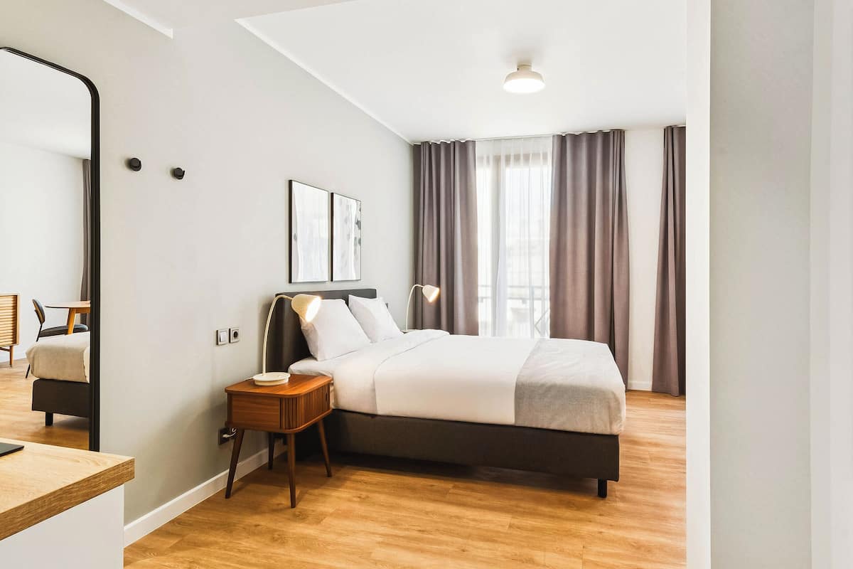 Moderni hotellihuone, jossa on suuri sänky, yöpöydät, peili ja näkymä ulos.