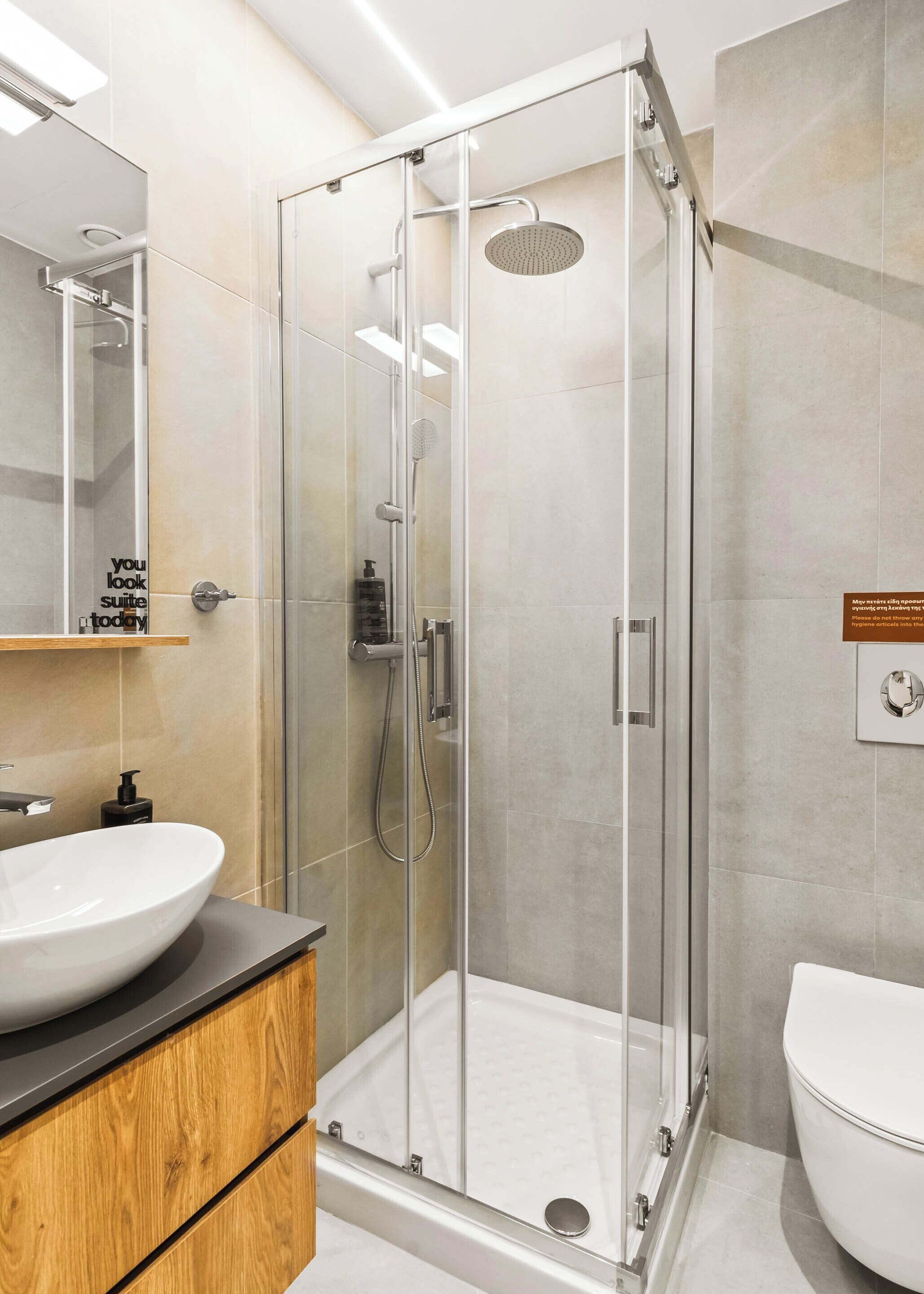 A modern bathroom with a glass-enclosed shower, a wooden vanity with a white sink, and a large mirror.
