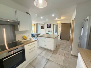 A modern kitchen with stainless steel appliances, a central island with a sink, and a dining area with chairs.