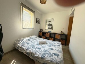 A bedroom with a bed, a window, a wall-mounted shelf with baskets, and a framed picture.