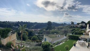 A view of a hillside with a well-maintained garden, a patio area with outdoor furniture, and a clear sky. - Quiet house on the Côte d'Azur (Cagnes-sur-Mer)