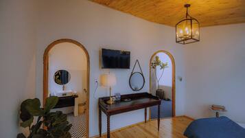 A bedroom with a wooden ceiling, a bed, a bedside table with a lamp, a TV mounted on the wall, and a mirror.