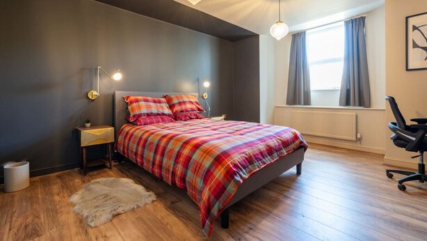 A bedroom with a bed, a nightstand, a chair, a fur rug, and a window with curtains. - Crookesmoor View, Sheffield (South Yorkshire)